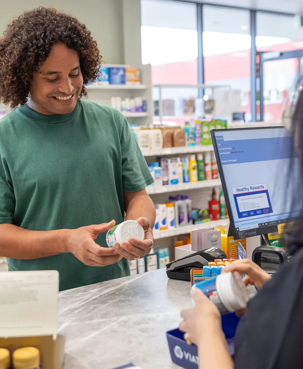 A smiling customer checking a medicine bottle at the pharmacy counter
