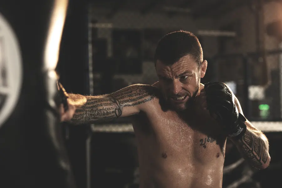 A tattooed fighter stretching his arm across his chest in a gym