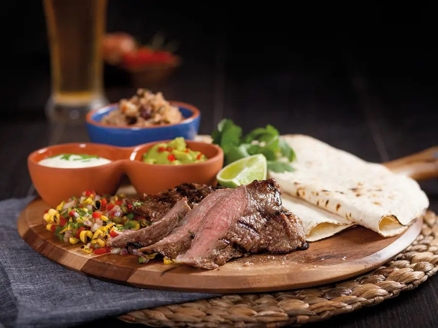 Sliced steak with salsa, beans and tortillas on a round board