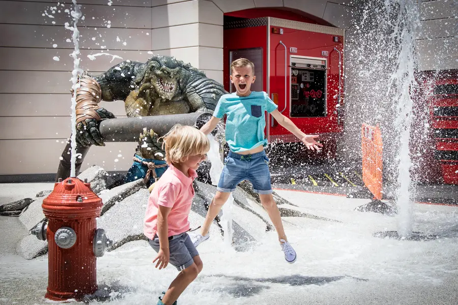 Children running through a fountain beside a giant villain sculpture