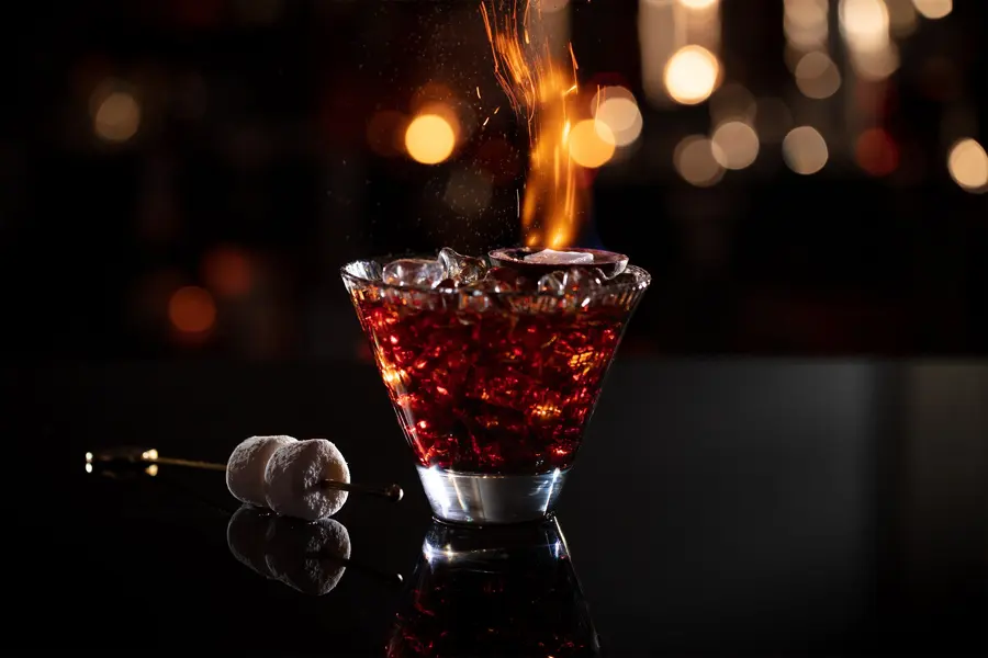 A flaming red cocktail on a dark bar