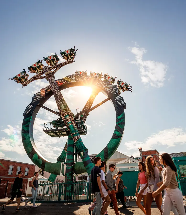 The Doomsday Destroyer ride spinning against the sun with guests walking below