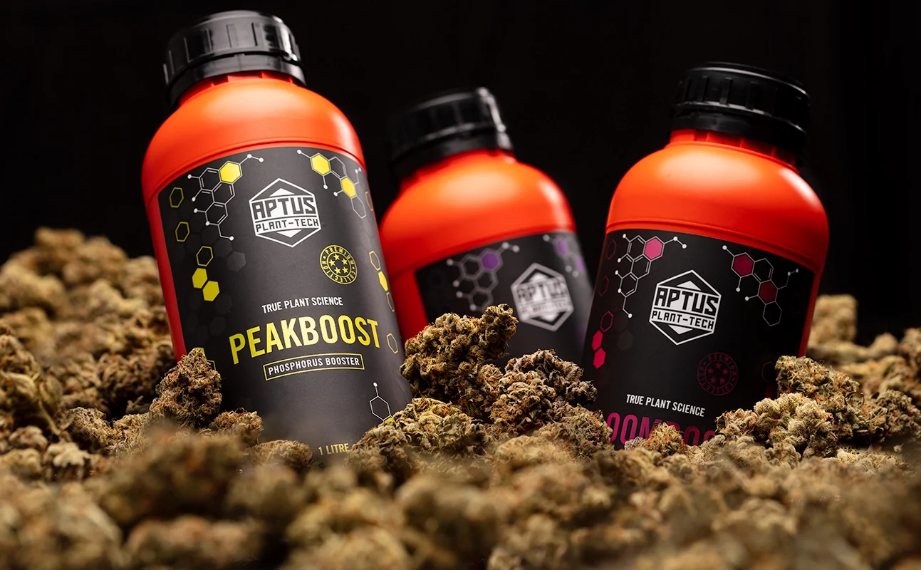 Three Aptus Plant-Tech bottles, Peakboost in front, half buried in dried flower against a black background