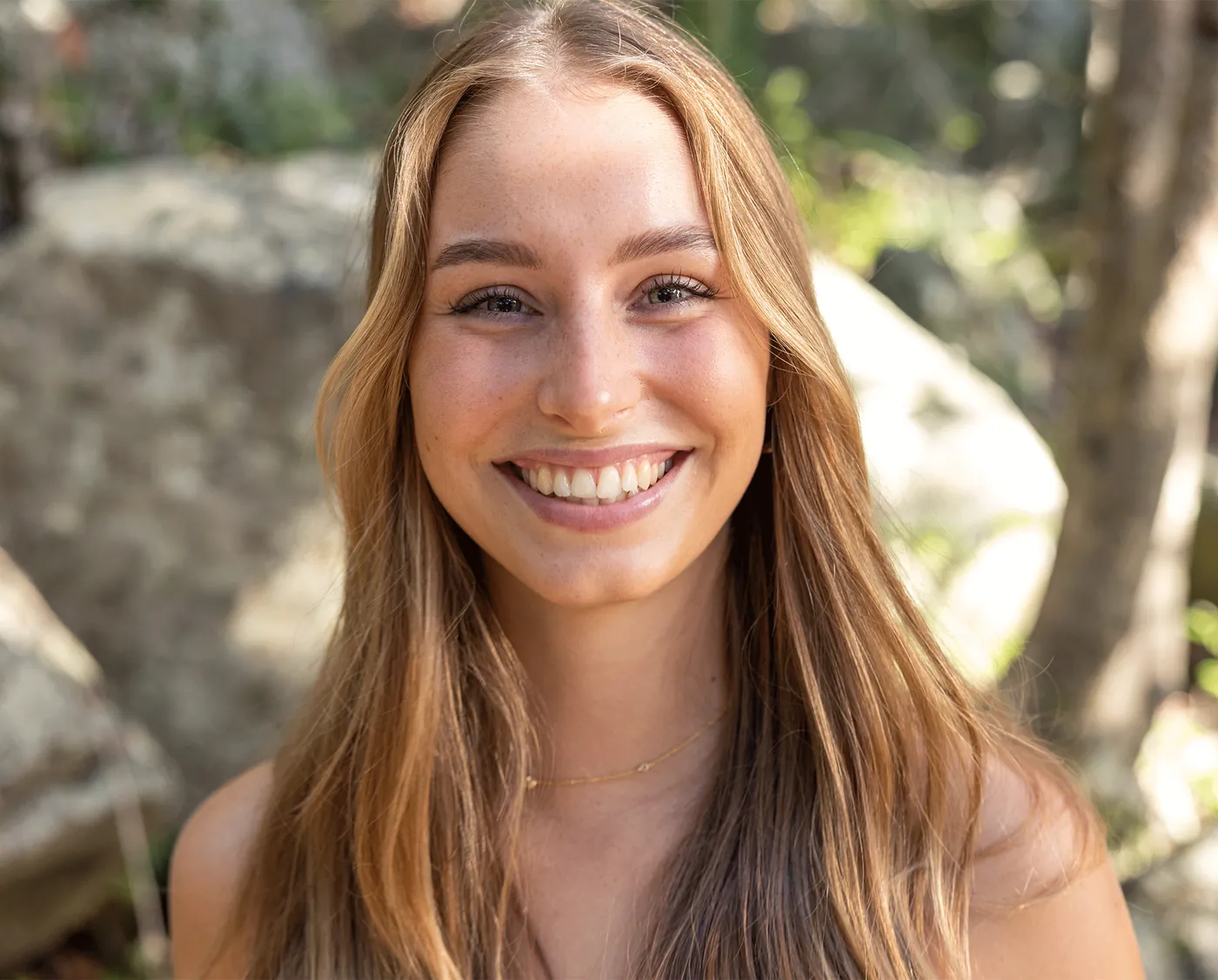 Portrait of a smiling young woman with long hair against soft rocks and greenery